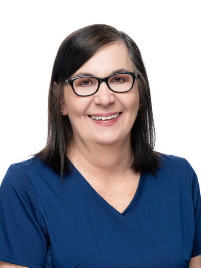A woman with straight dark hair and glasses smiles at the camera. She is wearing a navy blue V-neck top and is posed in front of a plain white background.
