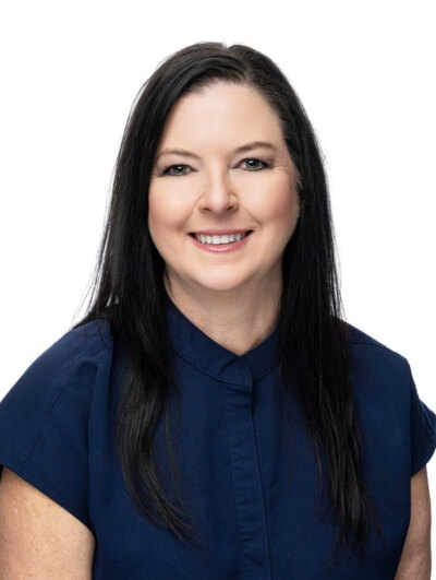 A woman with long straight dark hair and light skin, wearing a short-sleeve navy blouse, smiling at the camera against a plain white background.